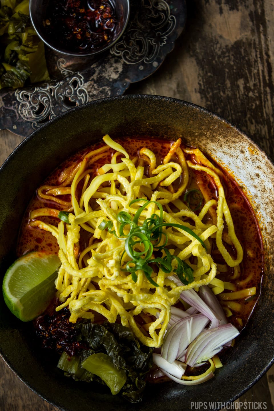 A large bowl of Khao soi topped with crispy egg noodles with a thai curry noodle soup
