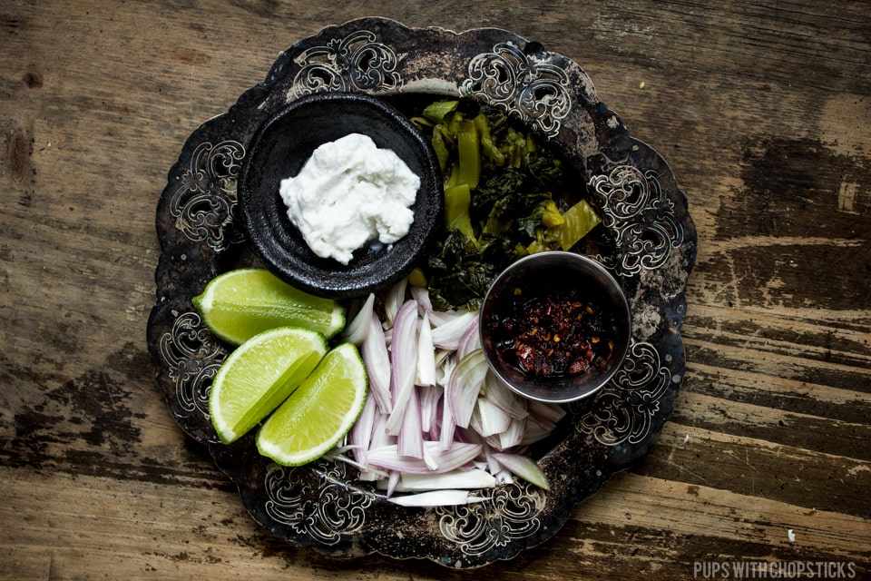 Toppings for khao soi laid out on a tray (limes, coconut cream, pickled mustard greens, chili oil, raw onions)