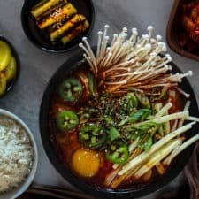 Spicy Kimchi Tofu Stew (Kimchi Jjigae) in a bowl with side dishes on a table