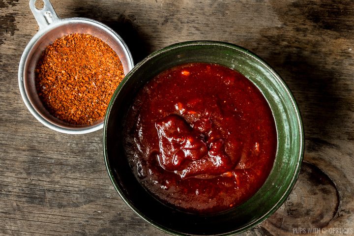 Sweet and spicy gochujang sauce in a green bowl with a side of chilli flakes