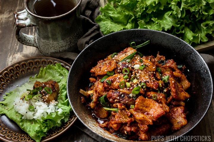 A large bowl of Spicy Korean Pork Bulgogi (Jeyuk Bokkeum) with a plate of lettuce with some rice and pork in it for wrapping