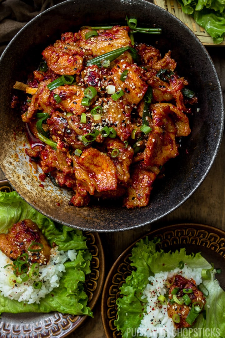A large bowl of Spicy Korean Pork Bulgogi (Jeyuk Bokkeum) with plates of lettuce with rice and pork on top ready for wrapping