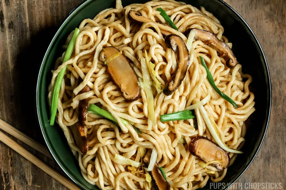 Longevity noodles (yi mein) in a green bowl, with wooden chopsticks.