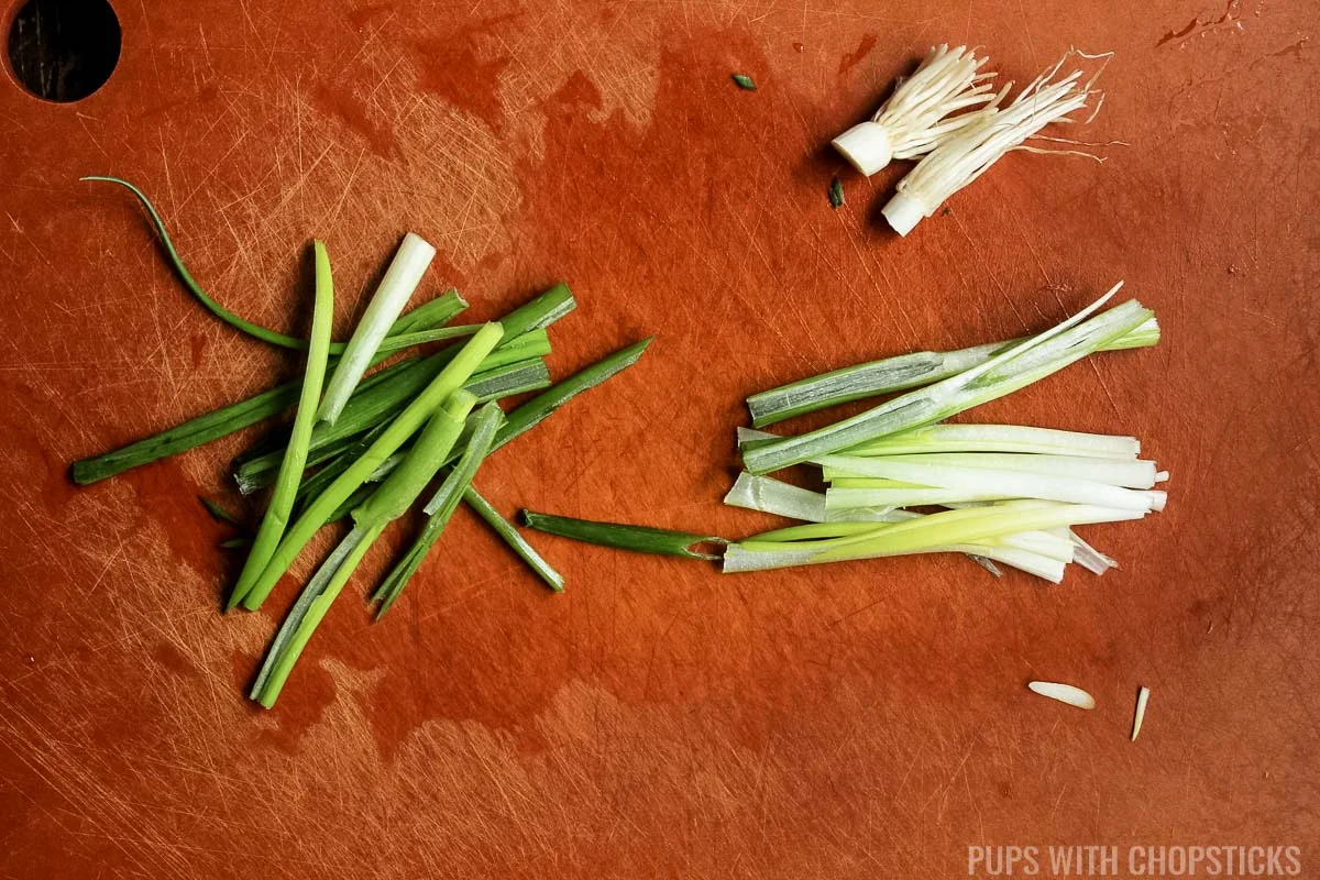 Chopping green onions in 2 inch lengthwise pieces on a cutting board.