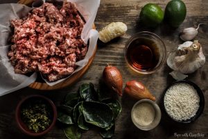 Lemongrass Pork Meatballs (Larb Style) ingredients laid out on a table (ground pork, galangal, lime, fish sauce, garlic, glutinous rice, shallots, kaffir lime leaves)