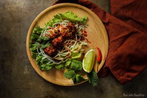 Lemongrass Pork Meatballs (Larb Style) in a piece of lettuce with some vermicelli noodles being made into a lettuce wrap on a table