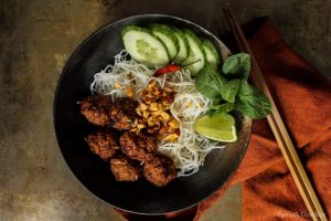 in a large bowl with vermicelli noodles, cucumbers and lime set on a table