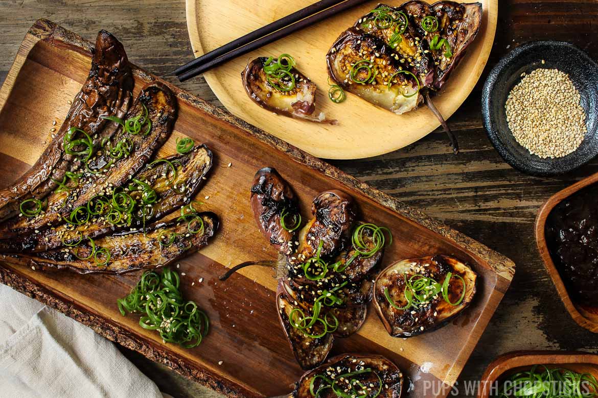 Miso eggplant fanned out on a wooden plate being served with sesame seeds and green onions
