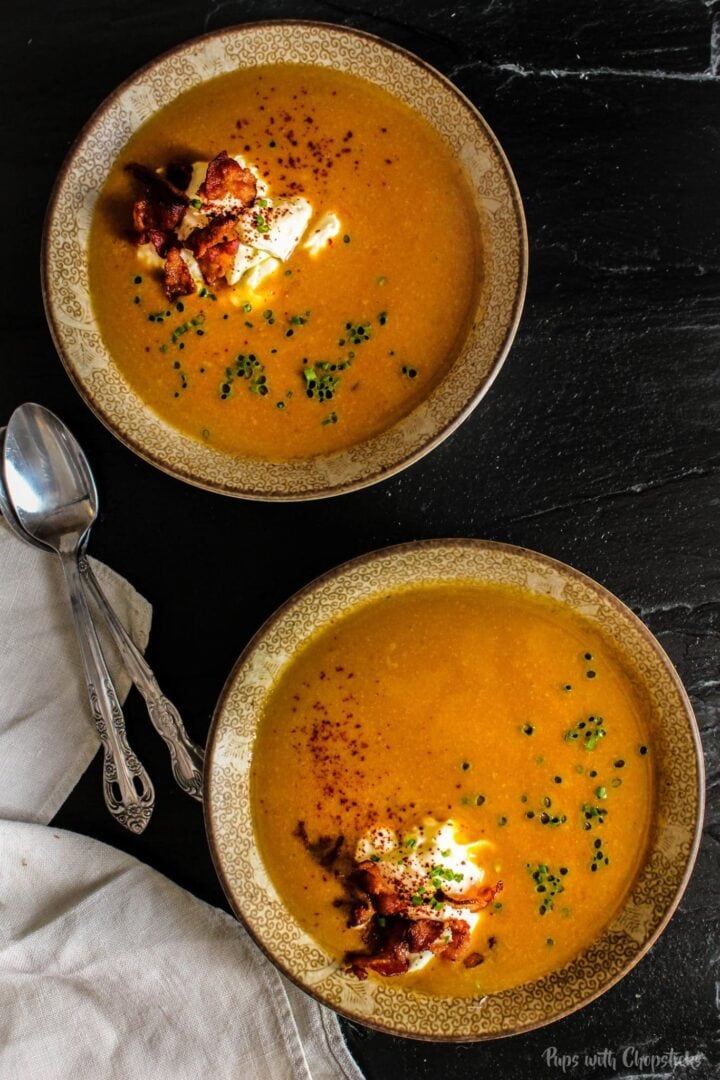 Two bowls of miso pumpkin soup garnished with crispy bacon, sour cream and chives.