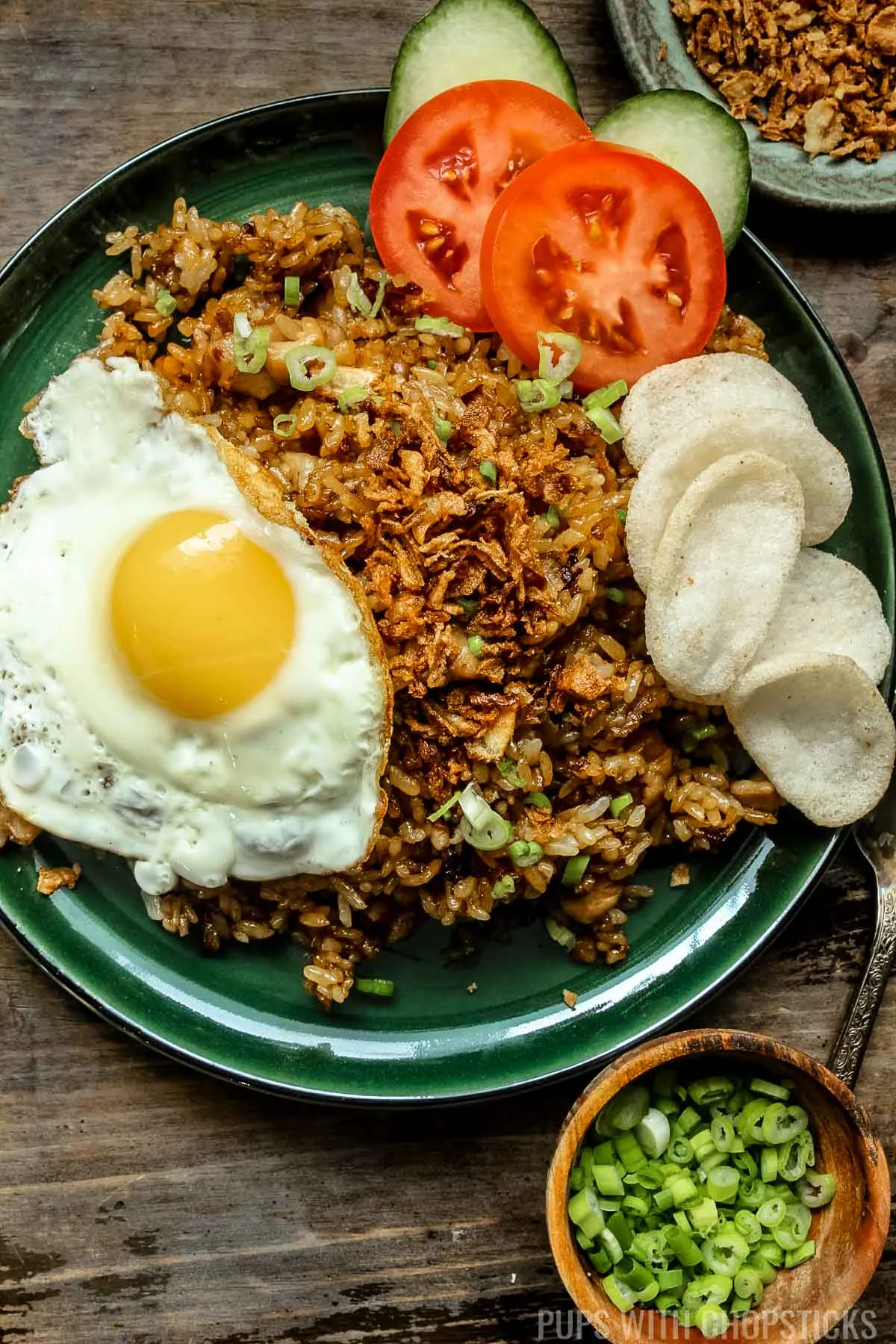 Nasi goreng (Indonesian fried rice) on a green plate with a fried egg, shrimp chips, fried shallots.