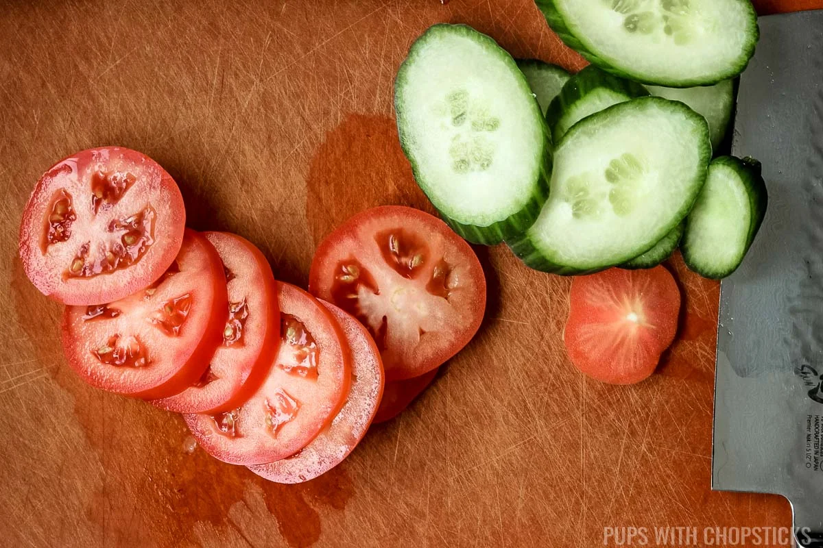 Tomatoes and cucumbers being sliced on a cutting board.