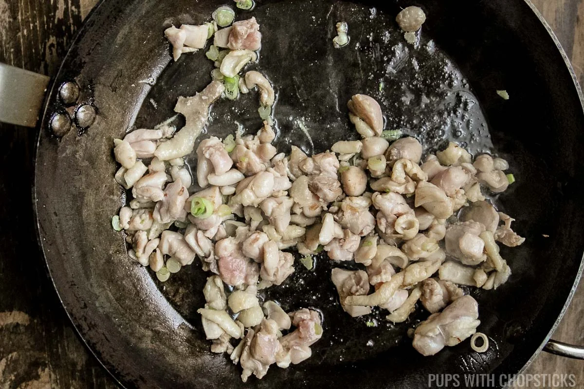 Stir frying chicken in a frying pan for nasi goreng.