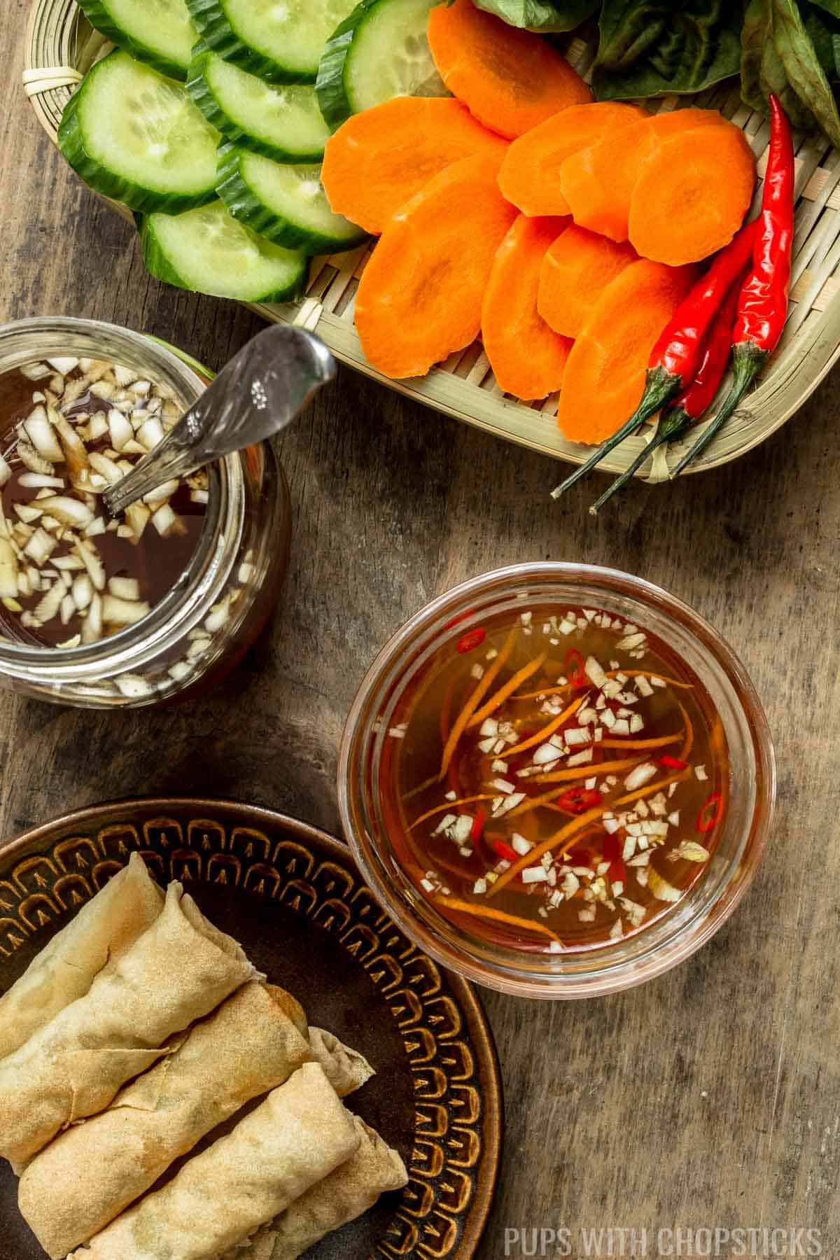 Vietnamese Fish Sauce Dipping Sauce (Nuoc Cham / Nuoc Mam) in a small bowl on a table with fresh vegetables and spring rolls