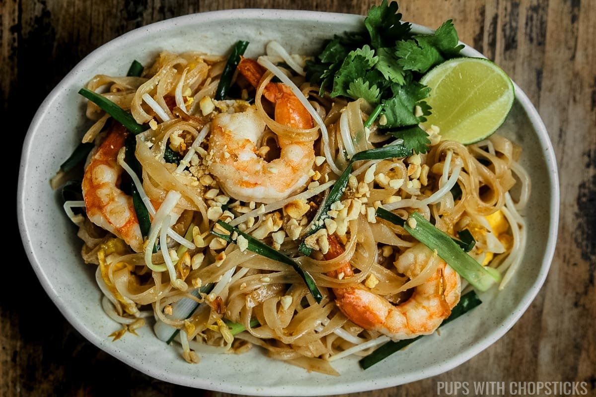 Pad thai with shrimp and peanuts in a beige oval plate on a wooden table.