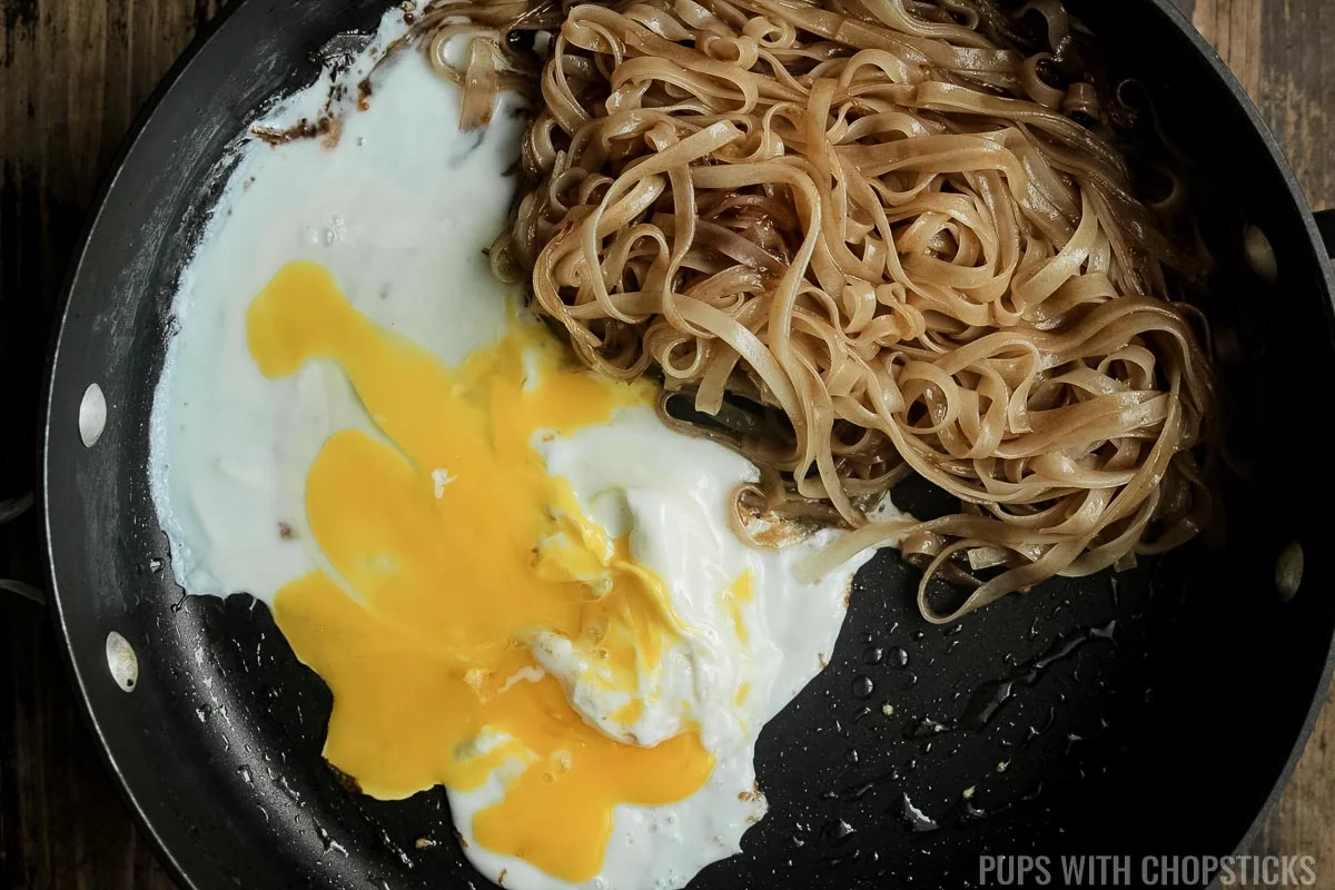 Eggs being scrambled with the pad noodles pushed to the side in the same frying pan