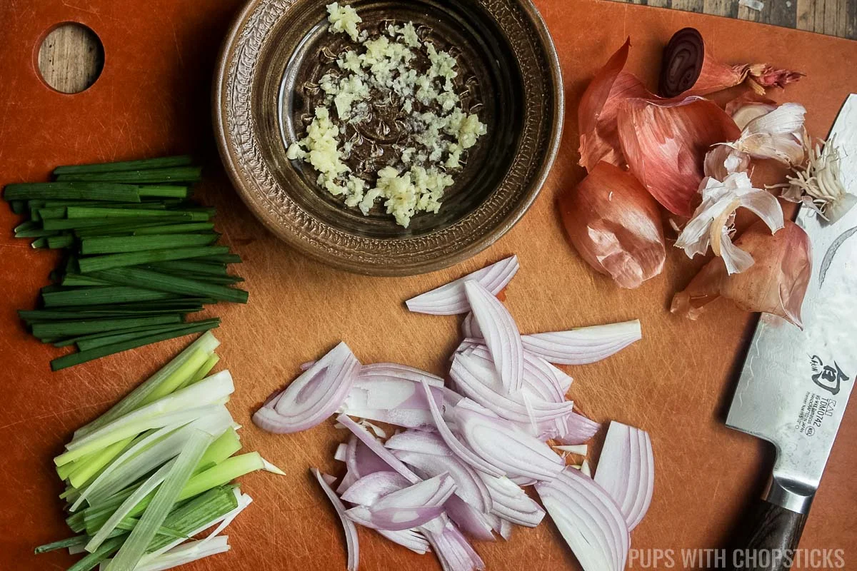 Green onions, garlic chives chopped, garlic grated and shallots sliced on a cutting board.