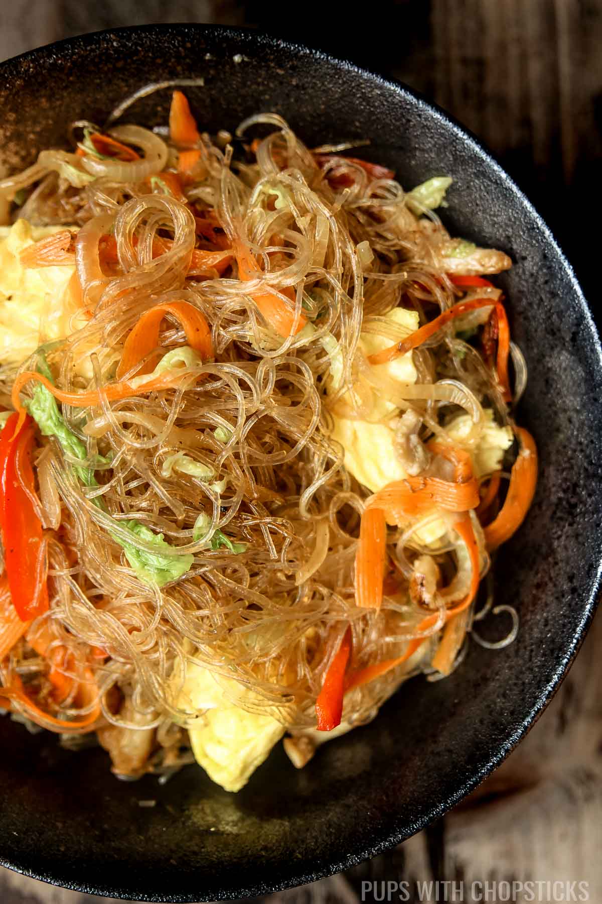 A bowl of pad woon sen (Thai glass noodle stir fry) in a large black bowl zoomed in.