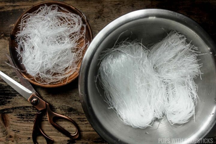 Bean thread noodles being cut with scissors into shorter 3 inch strands after it has been soaked