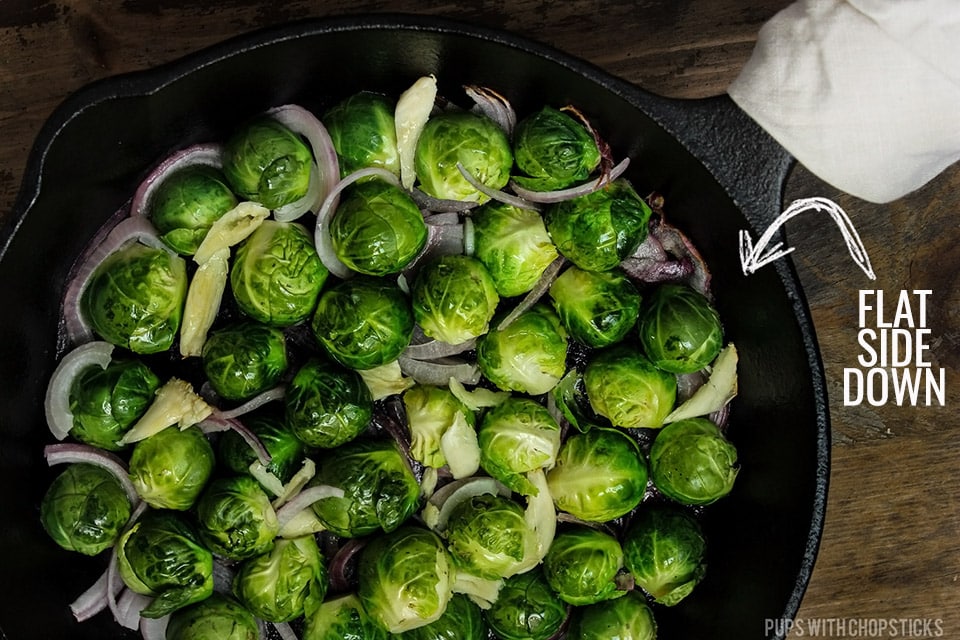 Brussels sprouts being pan fried flat side down in a cast iron pan