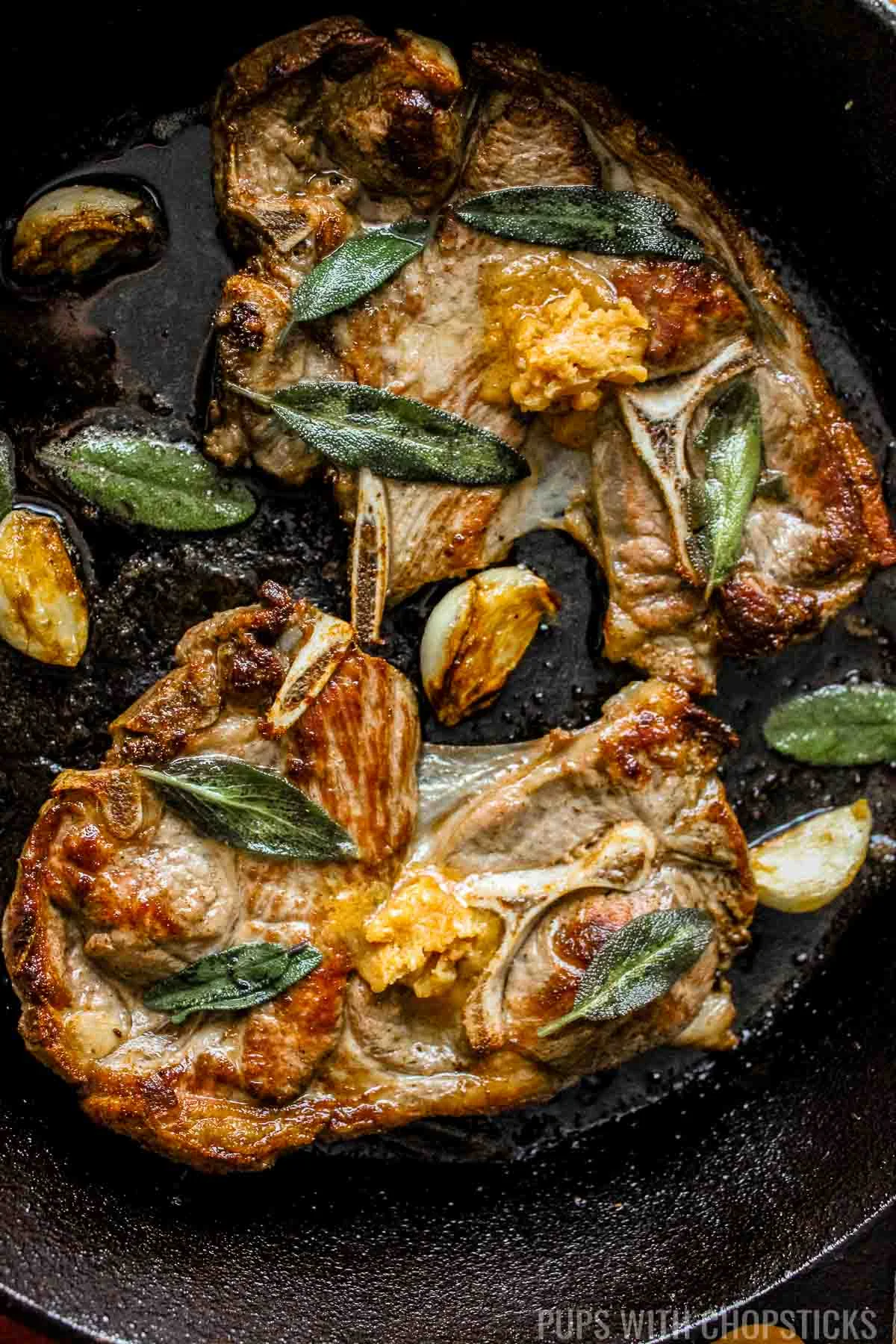 Miso butter pan fried lamb shoulder chops with garlic and sage on a cast iron pan