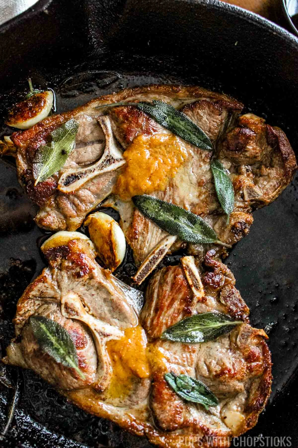 Miso butter pan fried lamb shoulder chops with garlic and sage on a cast iron pan