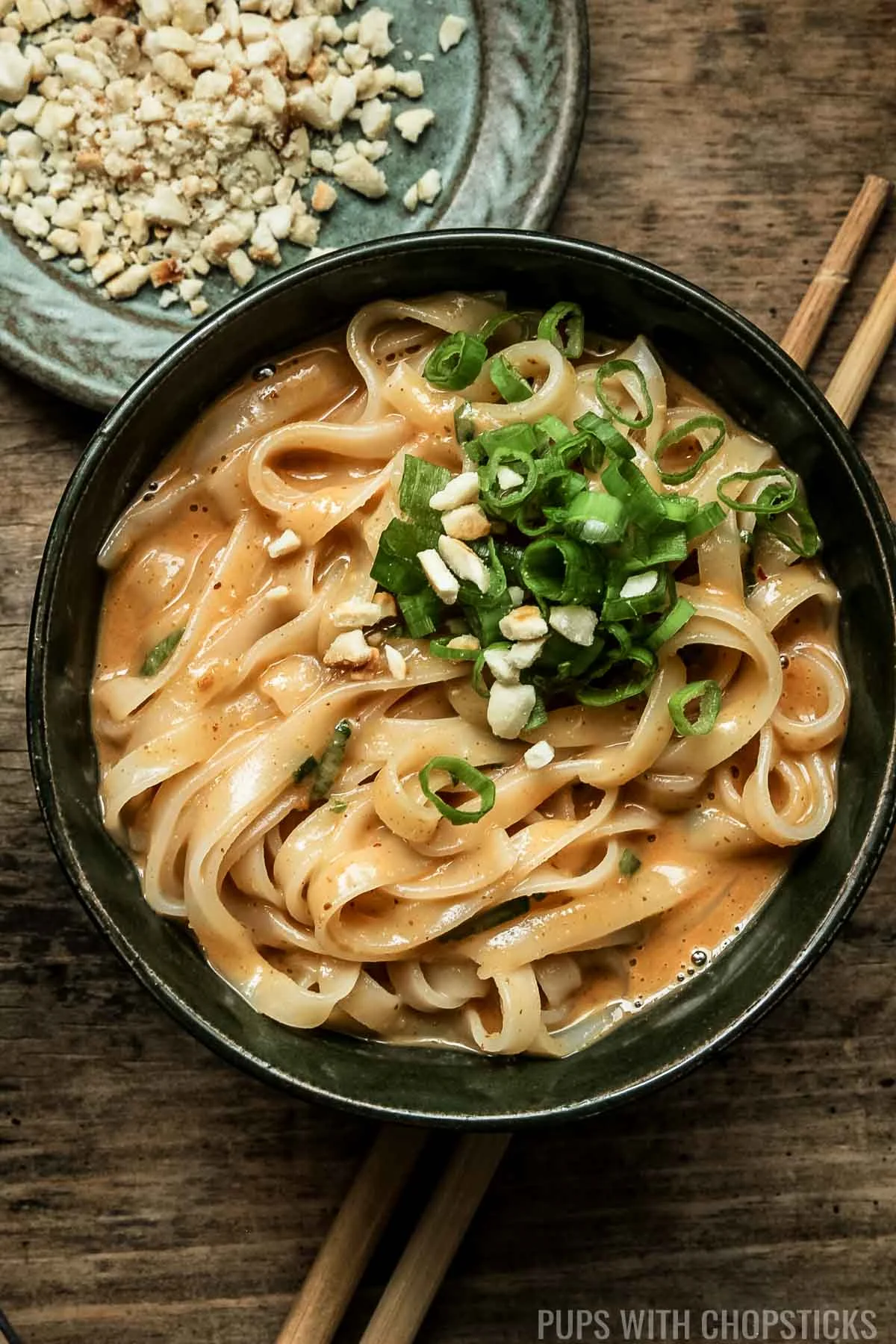 Thai peanut noodles in a green bowl served with crushed peanuts on the side