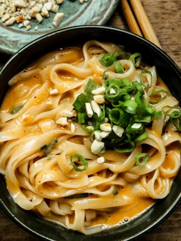 Close up of peanut noodles in a green bowl with green onions.
