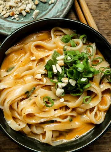 Close up of peanut noodles in a green bowl with green onions.