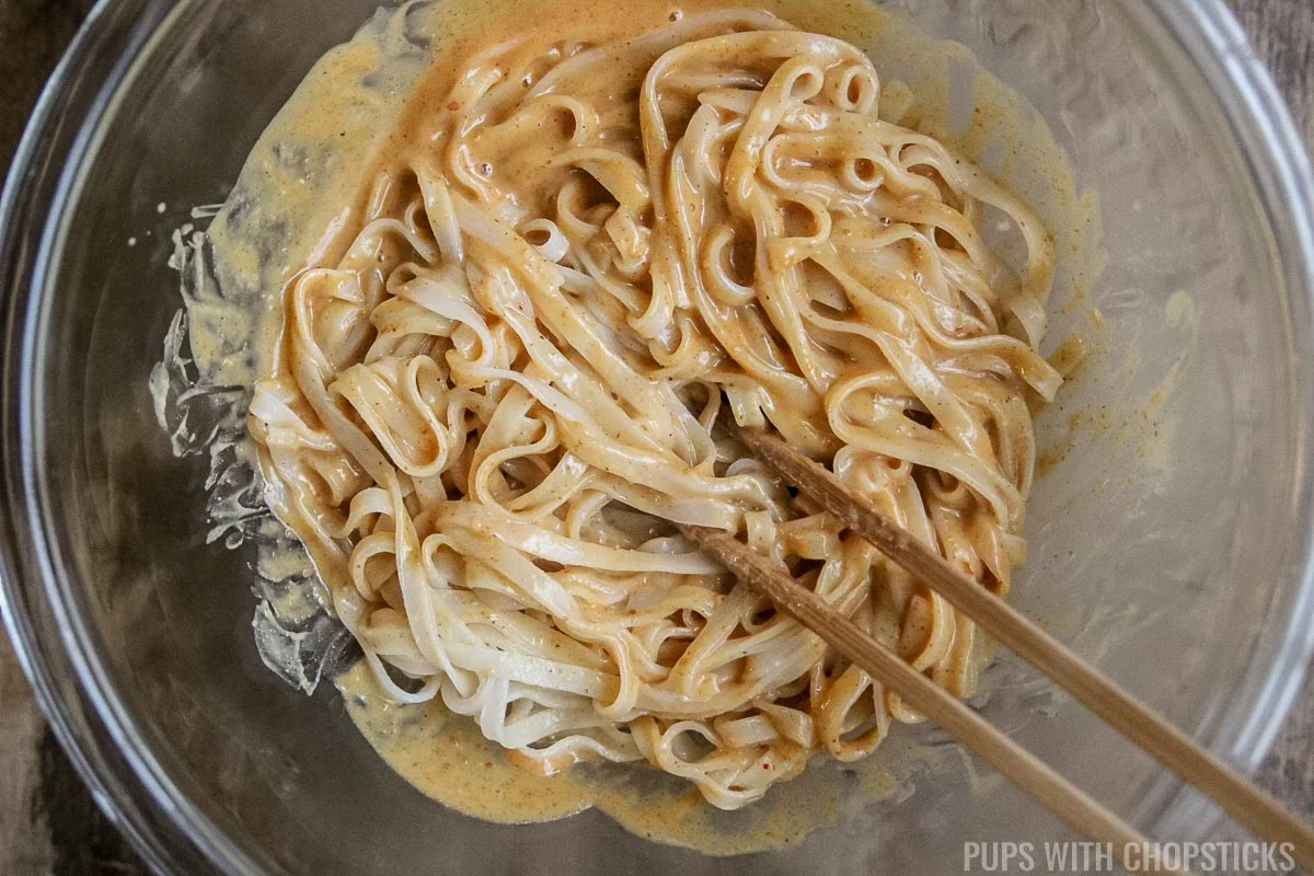 Mixing rice noodles in a glass bowl with peanut sauce