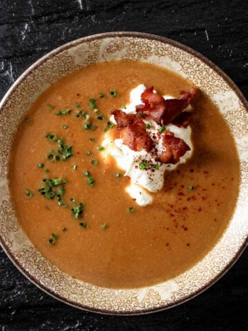 A small bowl of miso pumpkin soup garnished with bacon and sour cream