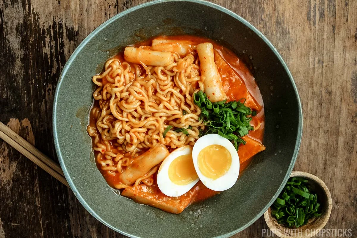 Rabokki served with soft boiled eggs in a green bowl.