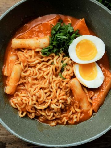 Closeup of Rabokki served with a soft boiled egg in a green bowl.