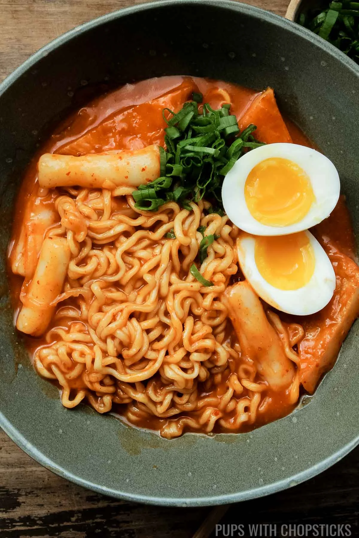 Closeup of Rabokki served with a soft boiled egg in a green bowl.