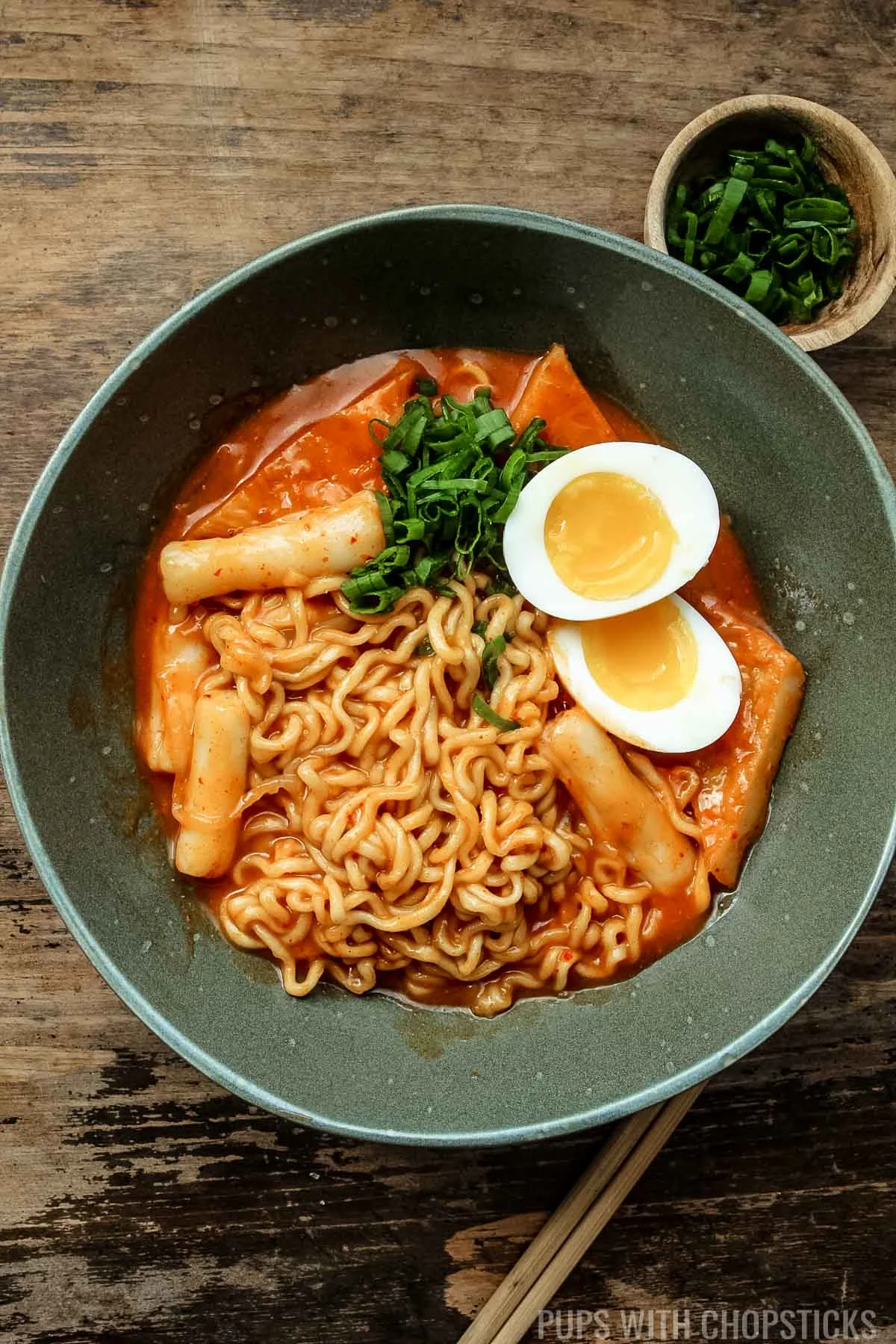 Rabokki served with a soft boiled egg in a green bowl with wooden chopsticks