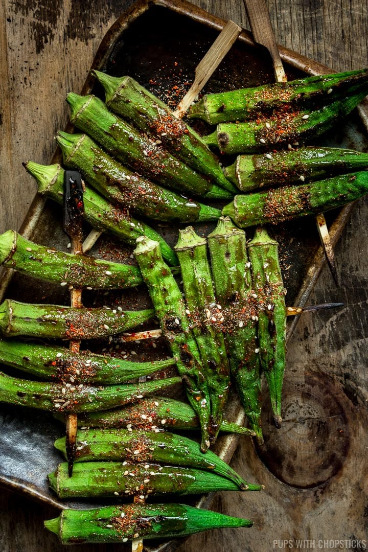 Skewered Roasted Okra sprinkled with spices and placed on a plate and set on a wooden table