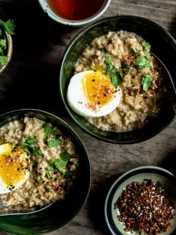 Two bowls of savory oatmeal on a table with a soft boiled egg on top and garnishes on the sides