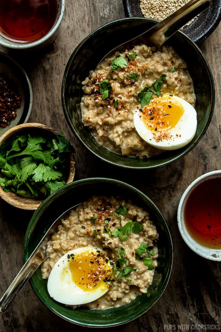 Two bowls of savory oatmeal with soft boiled egg on top served with tea on the side