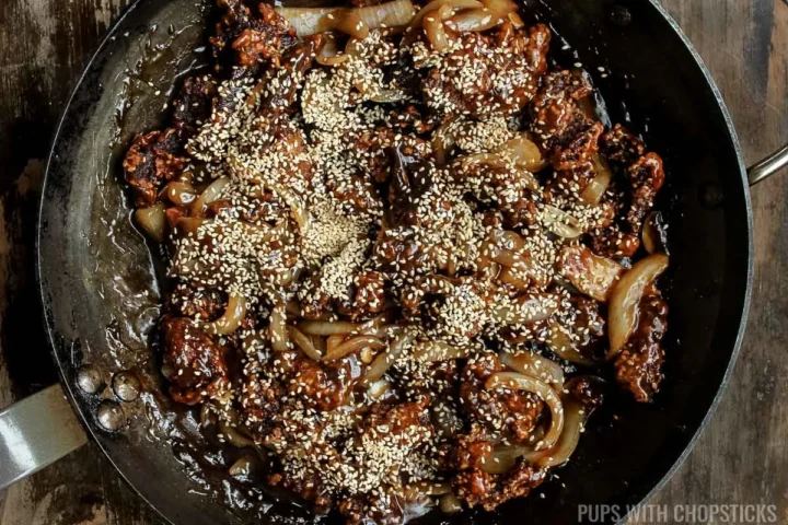 Add toasted sesame seeds to the final sesame beef dish in a frying pan.