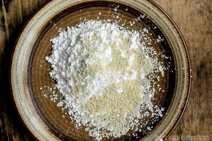 cornstarch on a plate mixed with raw white sesame seeds.