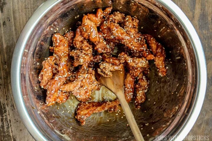 Sesame chicken being tossed in sauce and sprinkled with sesame seeds
