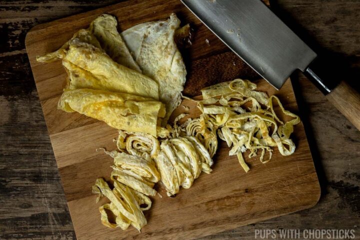 Thin sheets of egg omelette being sliced into egg ribbons for Singapore Noodles