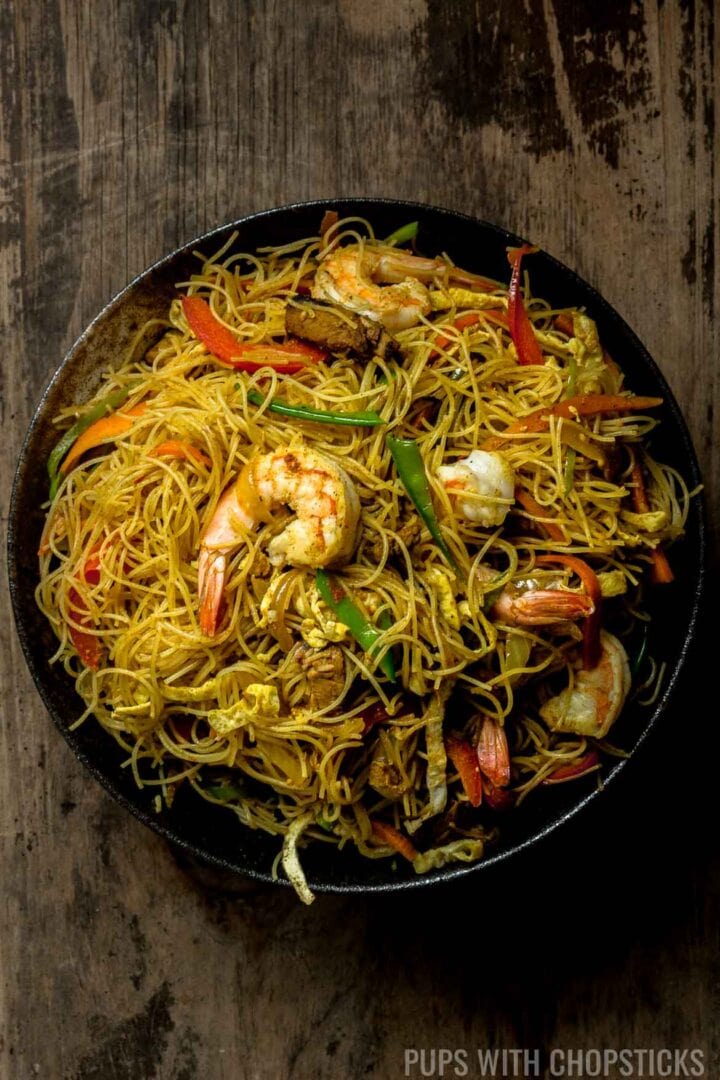 A large bowl of Singapore noodles, with shrimp, red pepper, snow peas, eggs and dry curried noodles