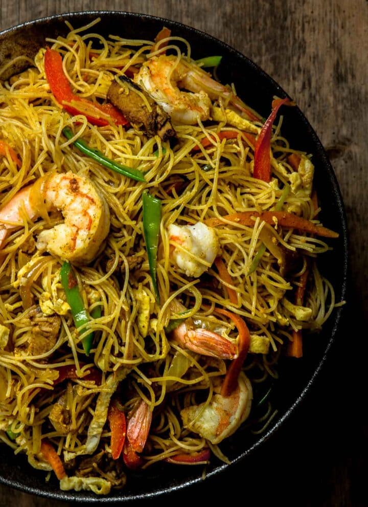 Dry curried Singapore Noodles in a large black bowl on a wooden table