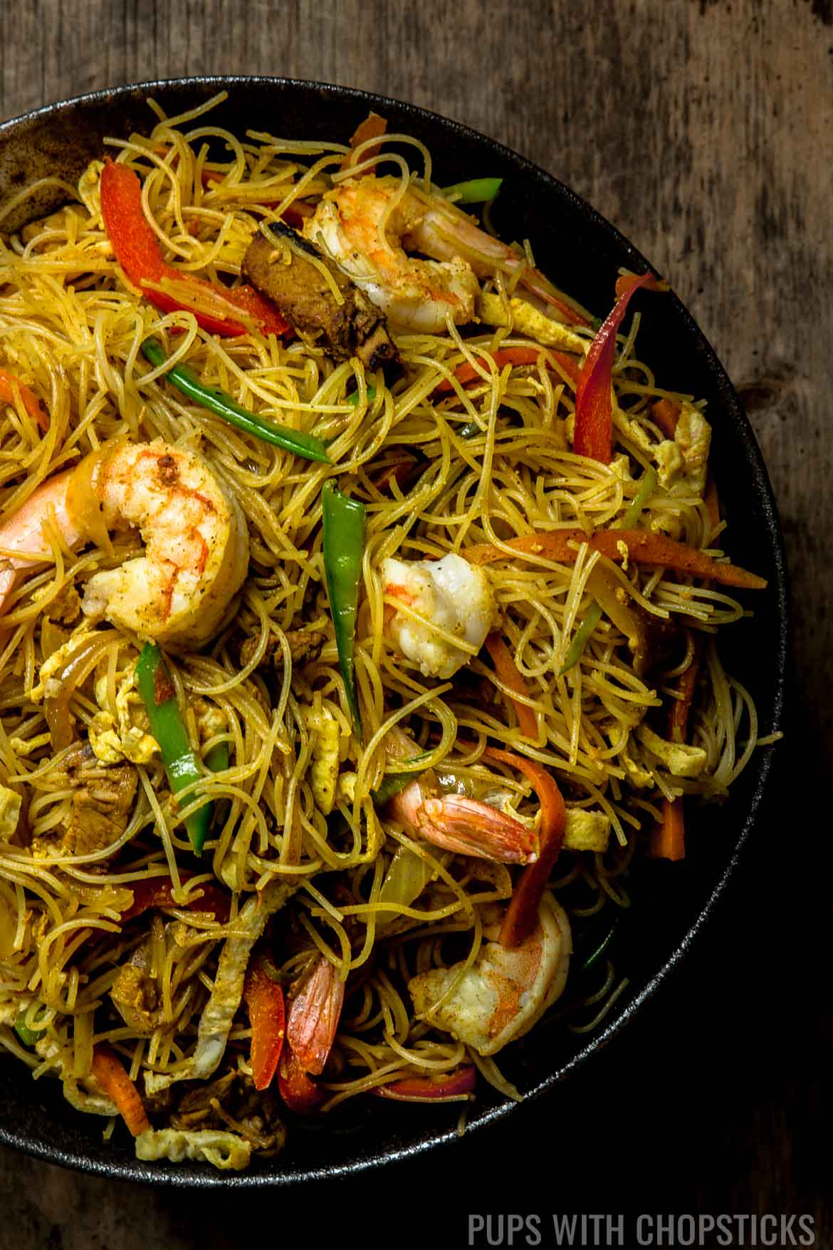 Dry curried Singapore Noodles in a large black bowl on a wooden table