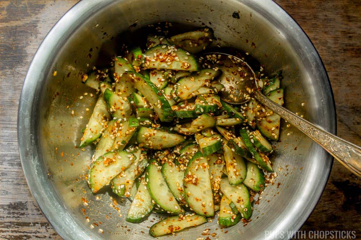 Close up of Korean cucumber salad (oi muchim) being mixed in a metal bowl with a metal spoon.