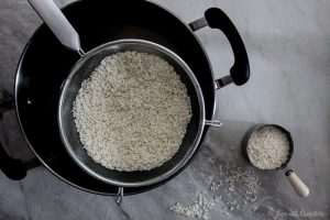 Rice being steamed in a pot for with a colander for Lao Crispy Rice Salad (Nam Khao)