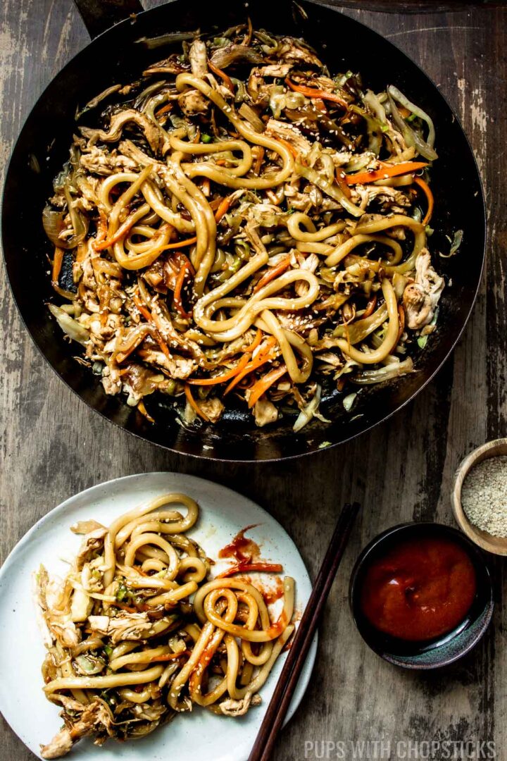 A pan with Stir Fry Chicken Teriyaki yaki udon, being served on a plate with hot sauce and sesame seeds