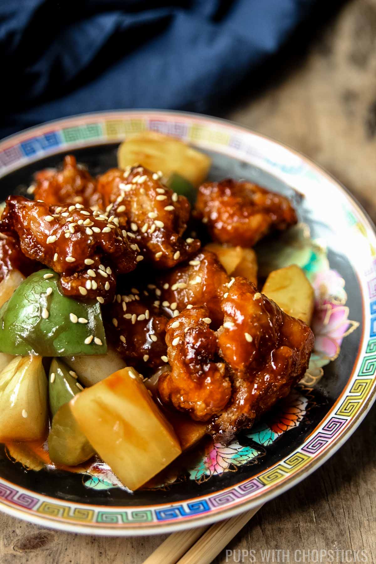 Close up of Hong Kong style sweet and sour chicken on a black plate with chopsticks