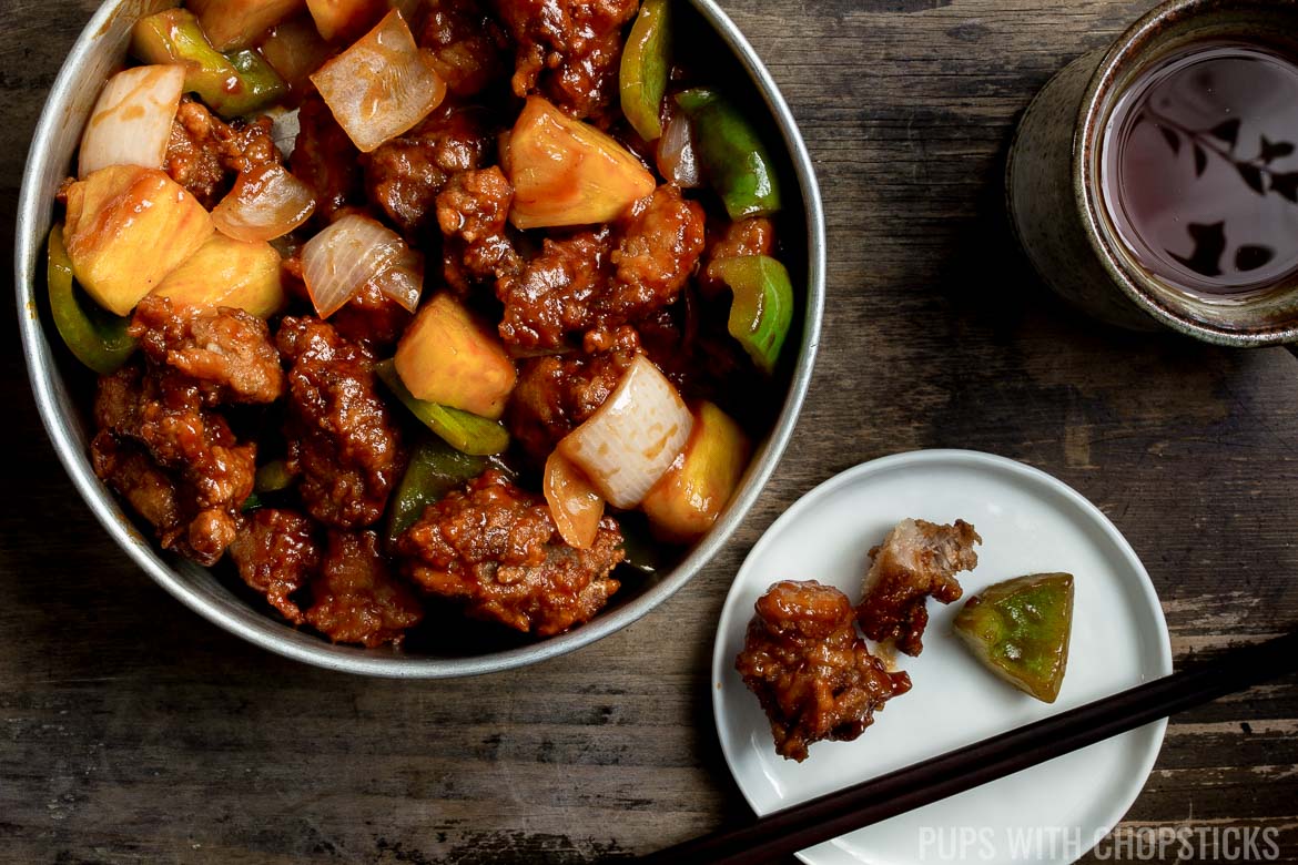 Sweet and Sour Pork In a large bowl with a small plate being eaten with chopsticks on a wooden table