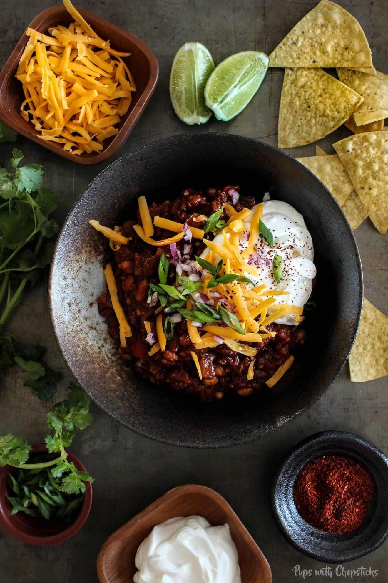 Sweet and Smoky Pineapple Chipotle Chili in a bowl with chips, lime wedges, sour cream and cheese on a table